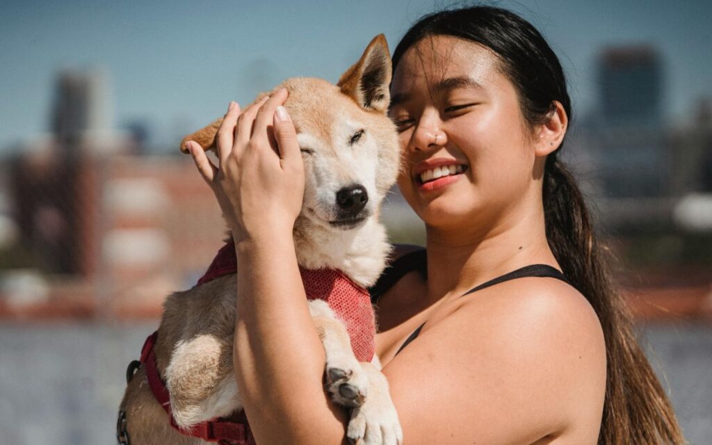 Woman holding a dog while smiling outdoors.