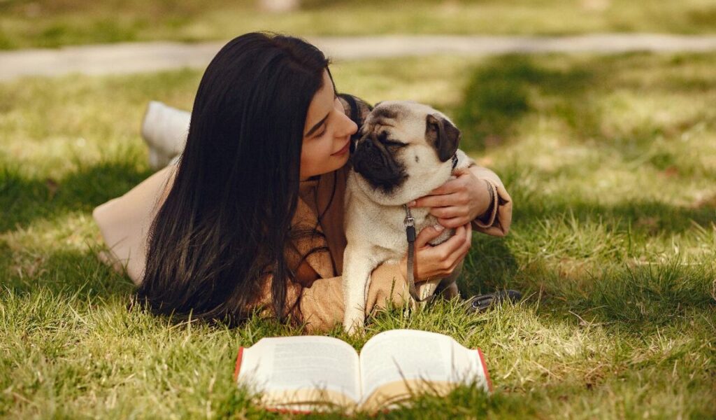 Woman cuddling with a pug on the grass.