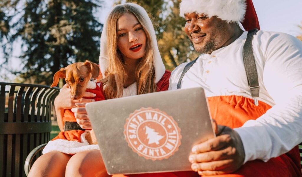 Two people in Santa outfits sitting with a small dog.