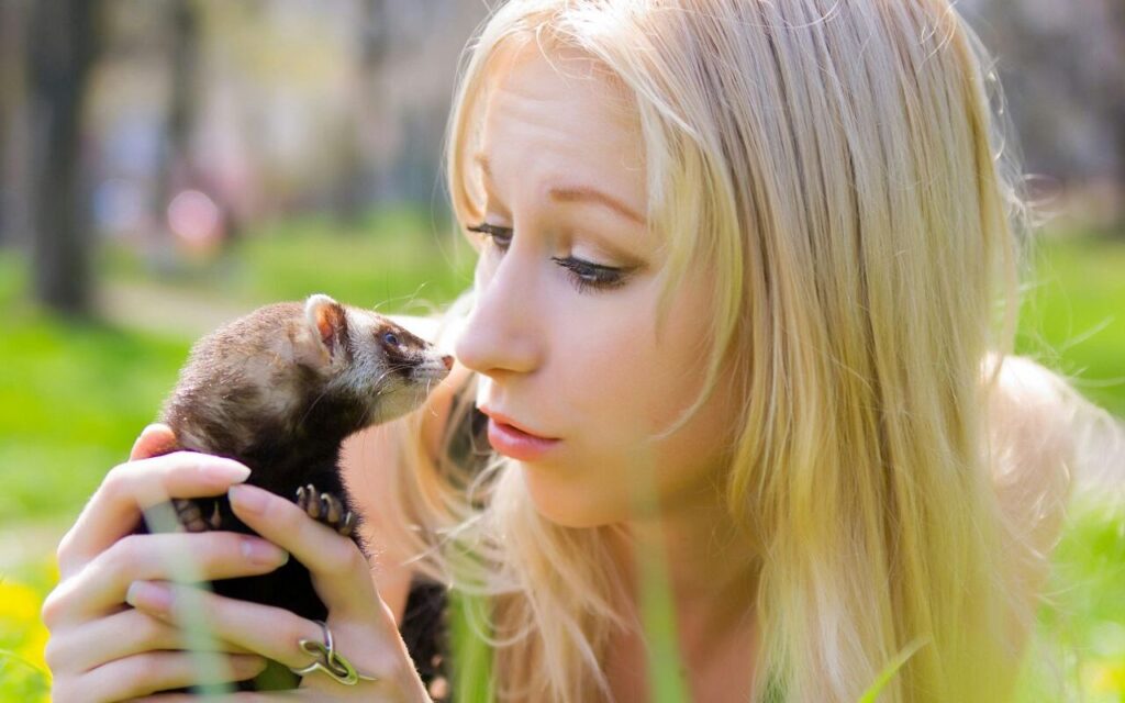 Woman holding a pet ferret outdoors.
