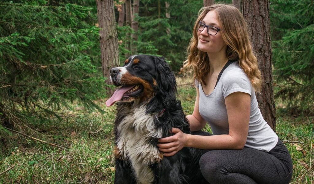 Smiling woman with a Bernese Mountain Dog in the forest.