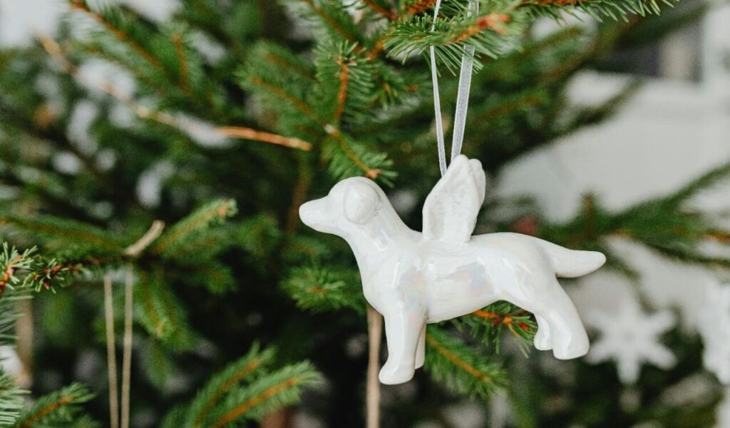 White ceramic dog ornament with wings hanging on a Christmas tree branch.