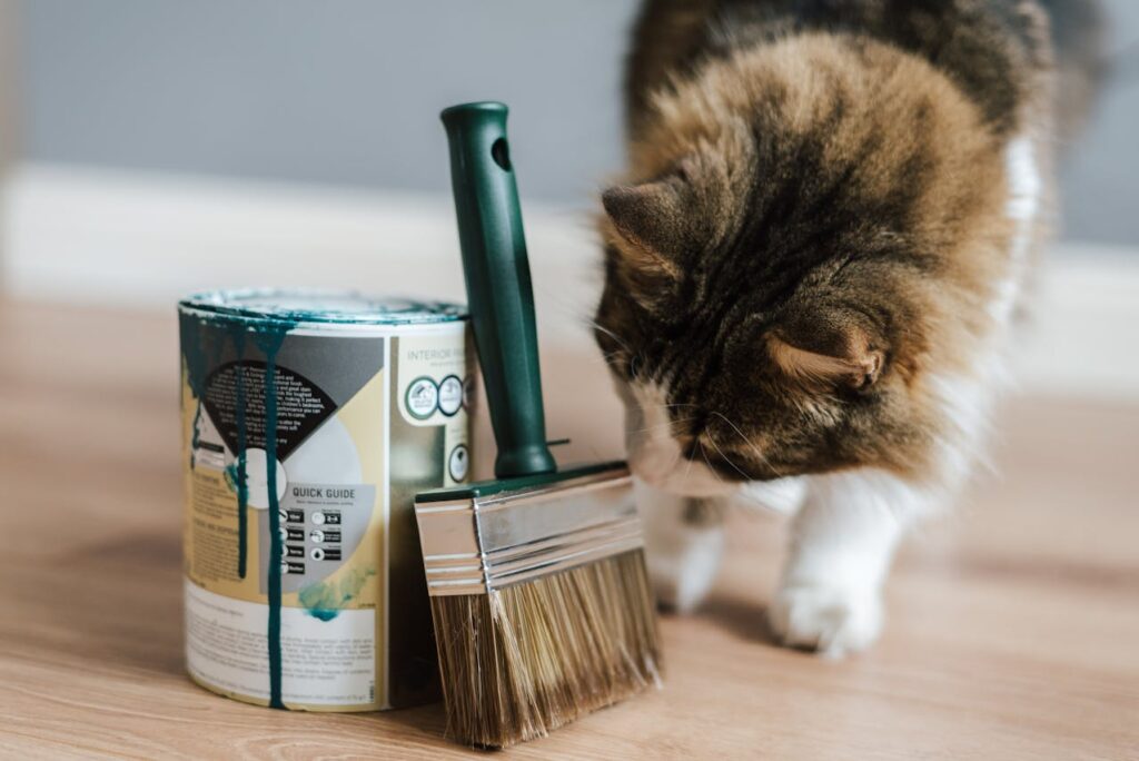 A fluffy cat curiously sniffing a paint can and brush on a wooden floor