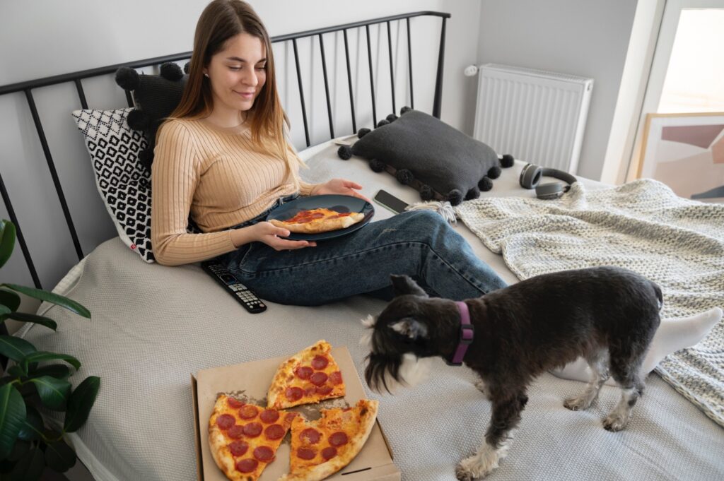 Young woman eating pizza on bed with Miniature Schnauzer