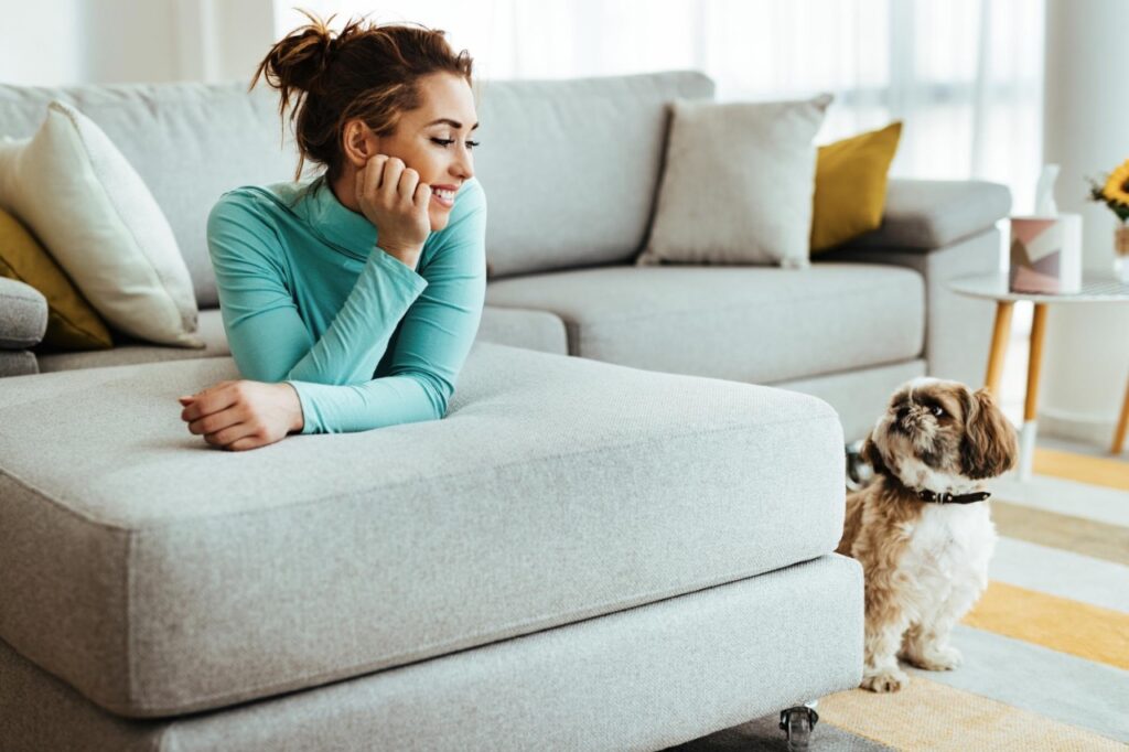 Happy woman lying down on sofa while relaxing with her dog at home