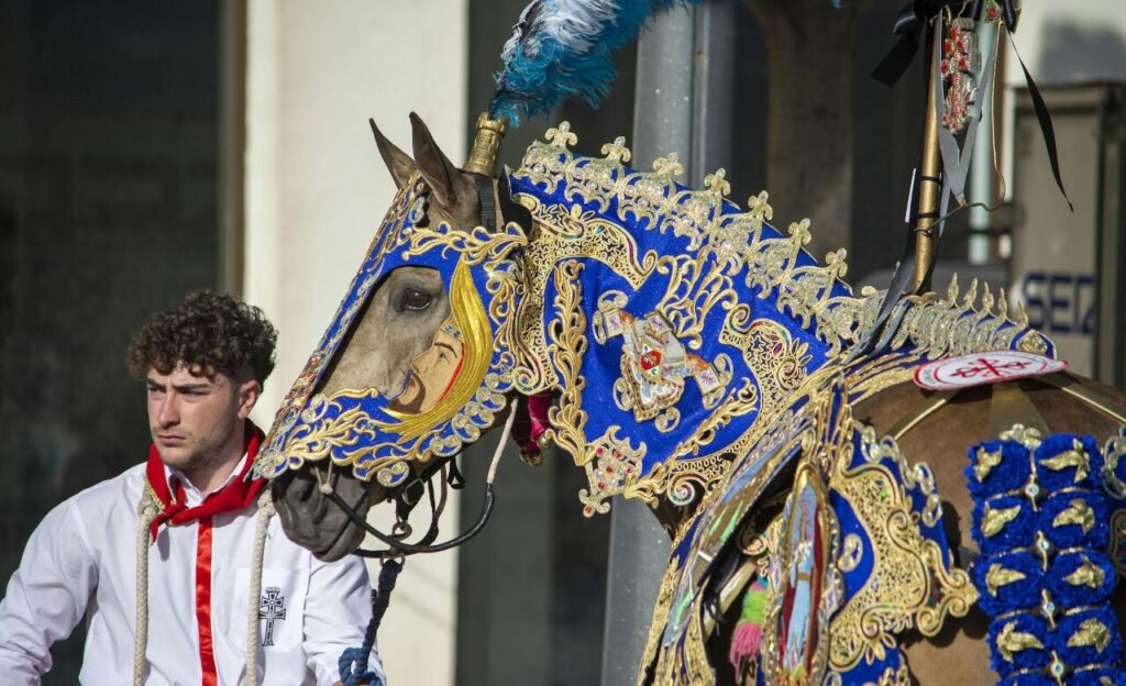 A decorated horse in ornate blue and gold attire with a man standing beside it.