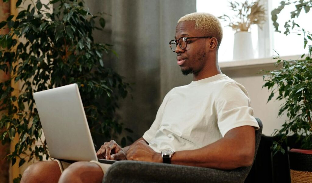 Man with Eyeglasses Using a Laptop while Sitting on a Chair