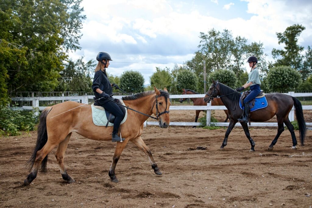 Women riding horseback on sand in paddock