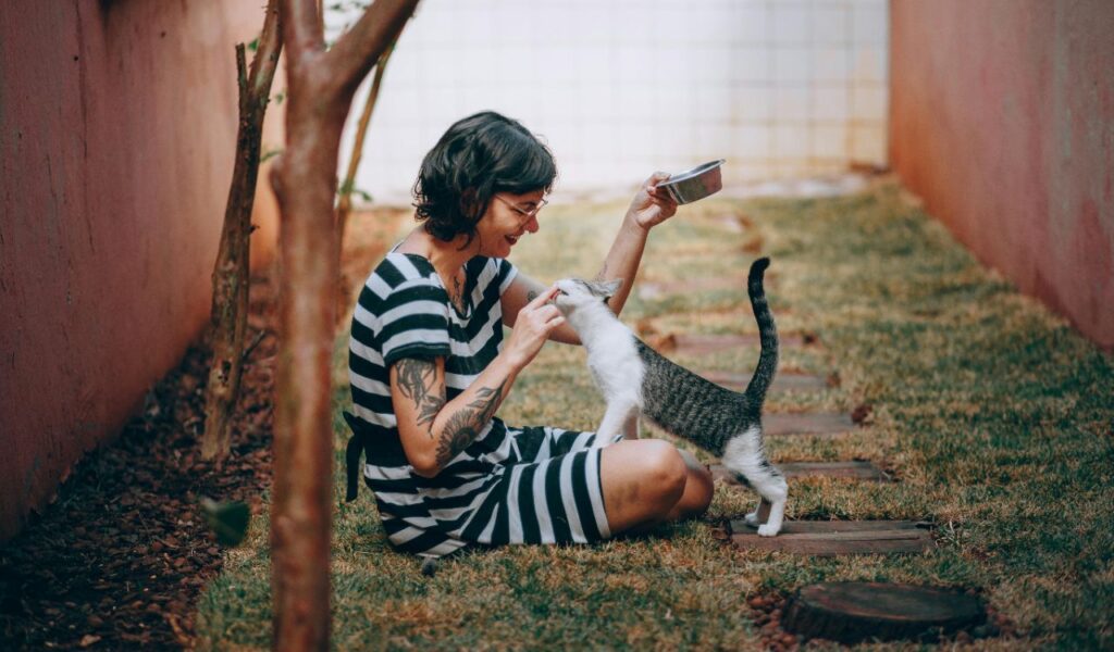 Smiling woman in a striped dress feeding a cat in a garden