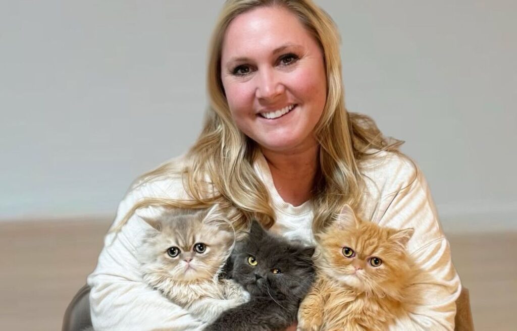 A woman holding three Persian kittens of different colors.